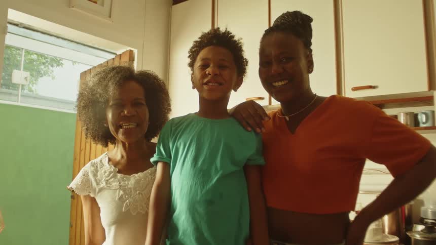 Three generations of a family smile while standing in the kitchen