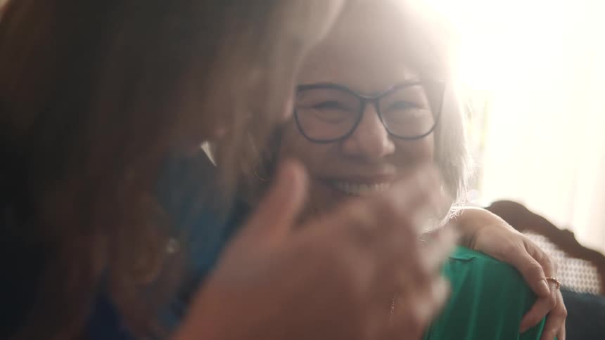 An elderly woman smiles warmly while being embraced by a younger person