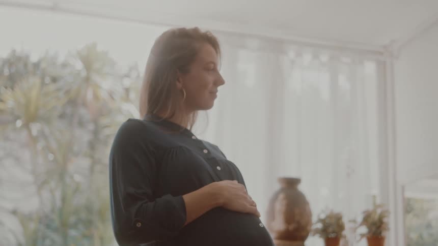 A woman is cradling her pregnant stomach in the room