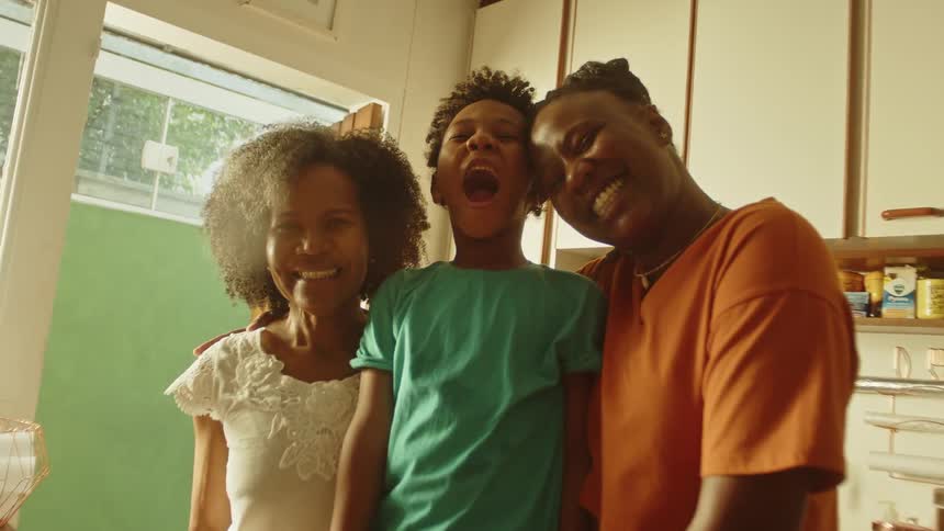 Three people smile together in a warm kitchen by fresh fruit