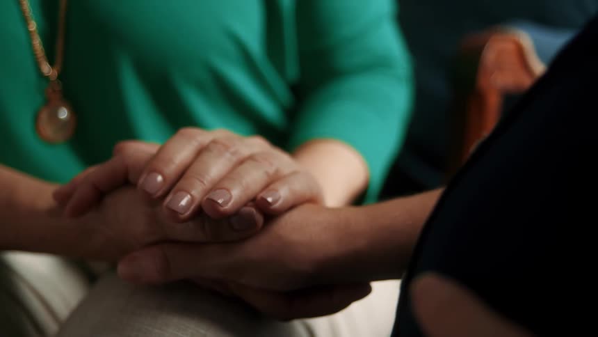 Close up of two women holding hands while sitting indoors