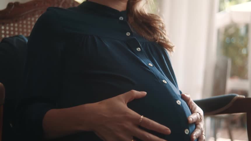 A pregnant woman is sitting and she is happy as she is running her hands over her belly