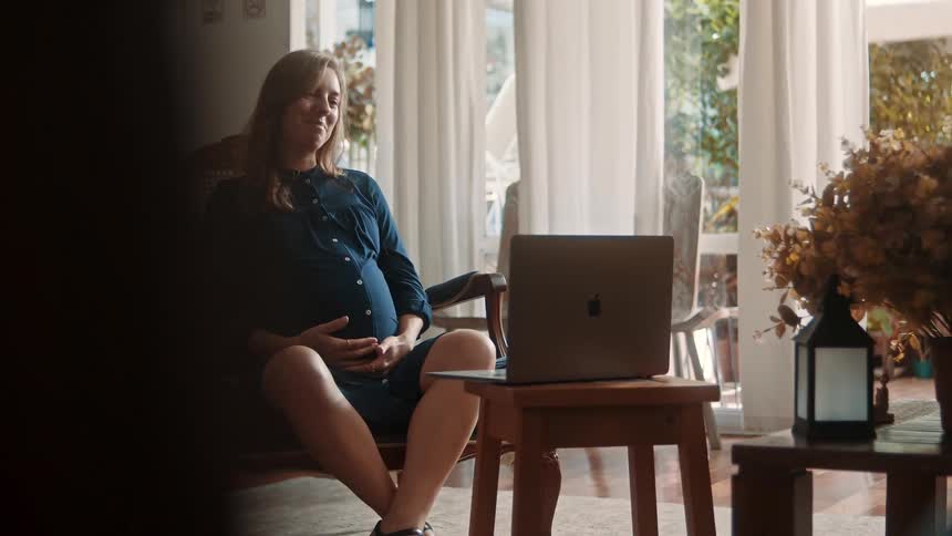 A pregnant woman is talking with someone on her laptop