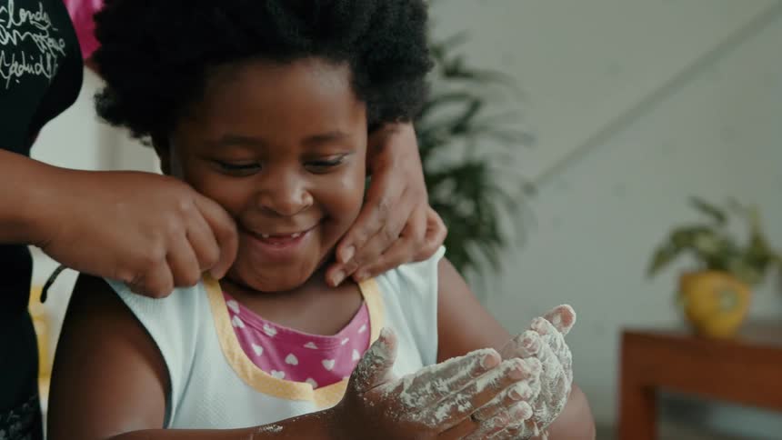 A mother pinches her daughters cheeks while they cook