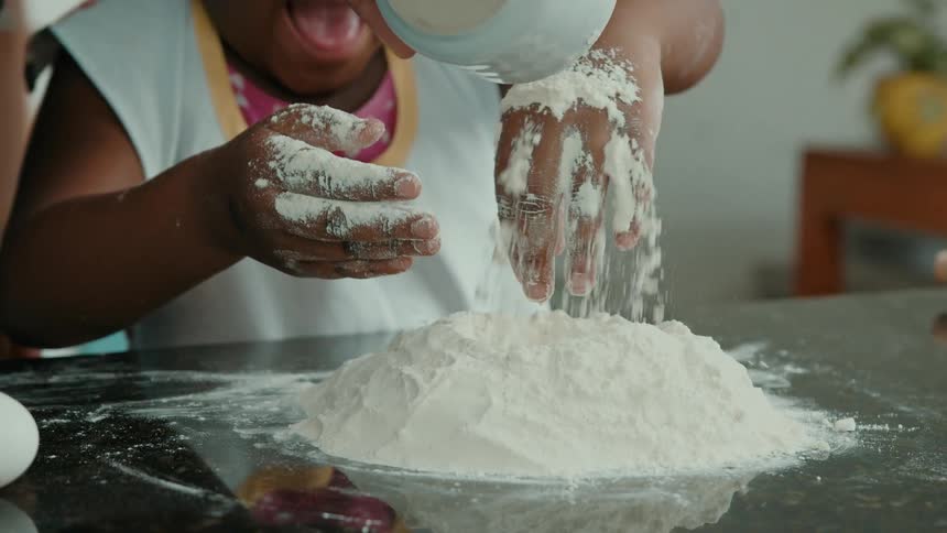 A hand pours flour onto a child flour covered hands
