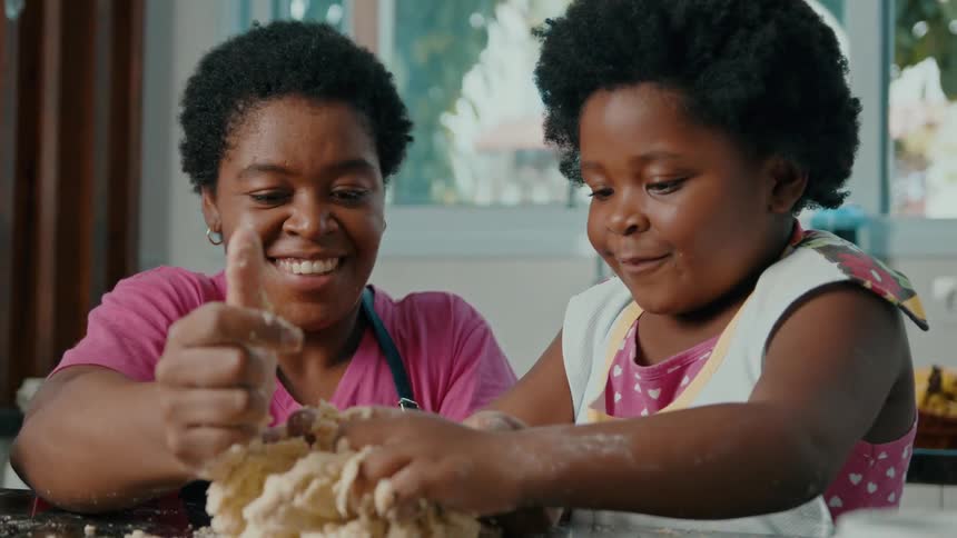 A smiling woman and a young girl joyfully knead dough together in a kitchen