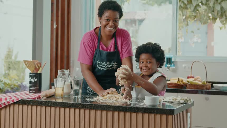 A woman and a young girl joyfully make dough together in a kitchen