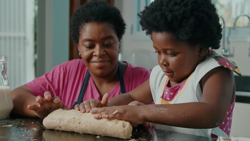 Mother smiles while watching her daughter roll fresh dough on the counter