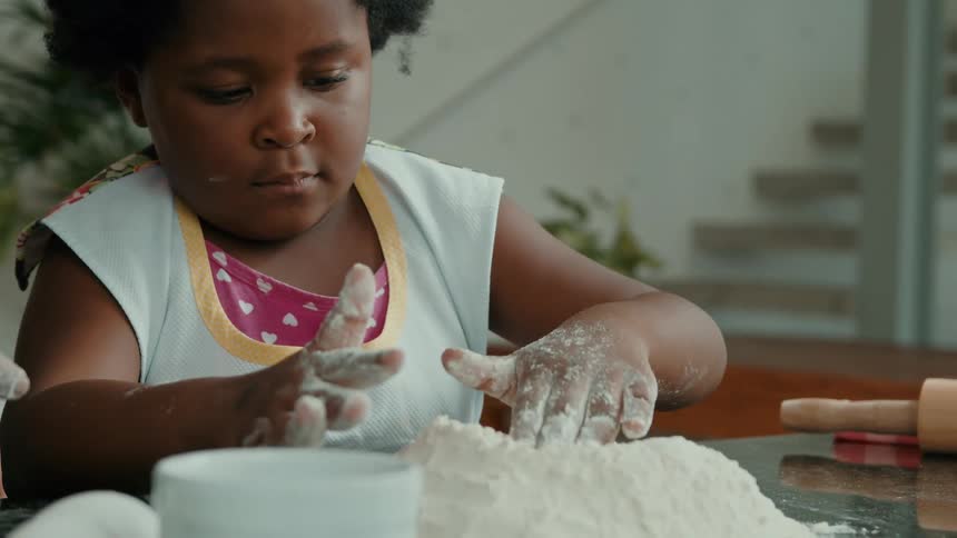 A girl is patting down the flour on the counter