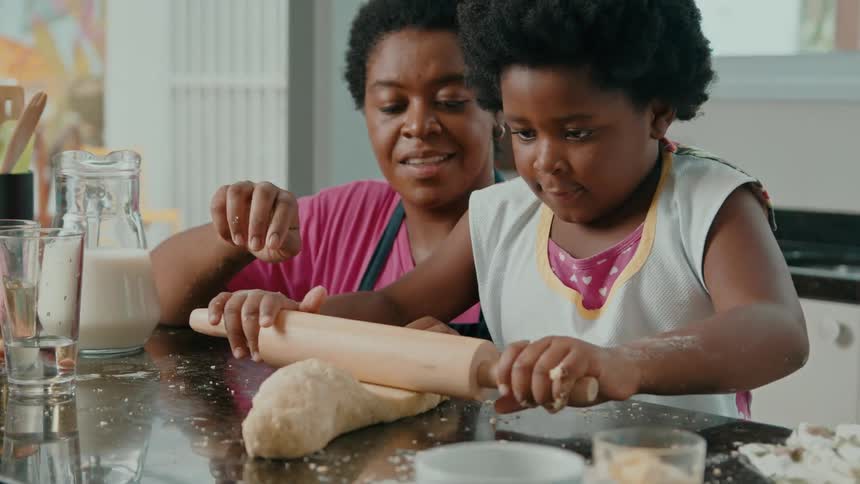 Child rolling dough with mother help in a kitchen