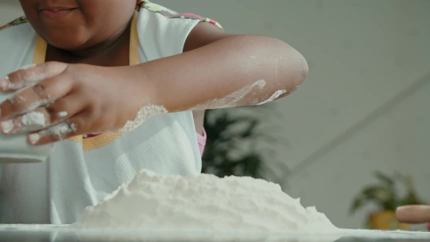 Adult helps young girl pour whisked eggs into a flour well on the counter