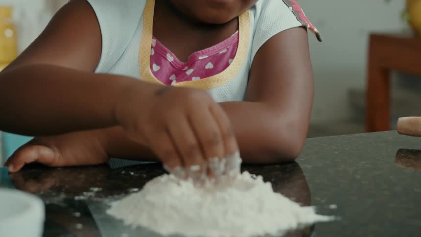 A child plays with flour dough on the kitchen countertop at midday