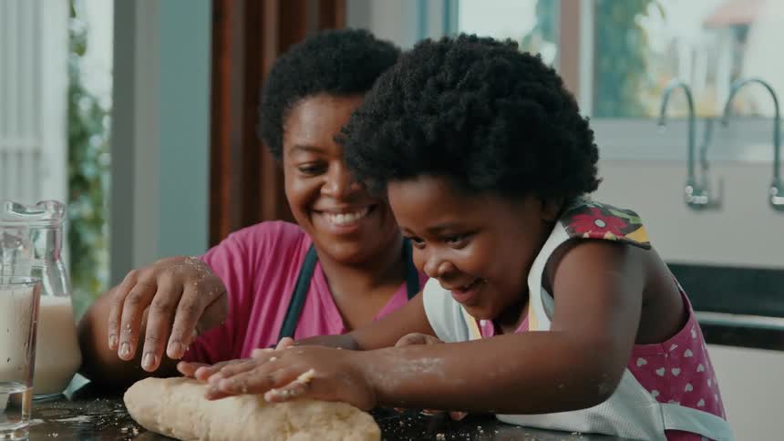 A mother helps her daughter knead dough at the kitchen counter with joy