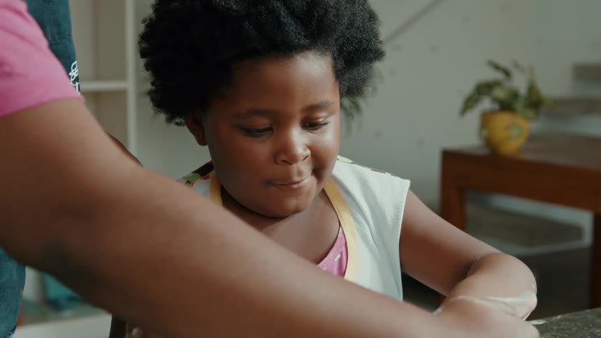 A child happily cuts dough with their hands while baking assisted by an adult