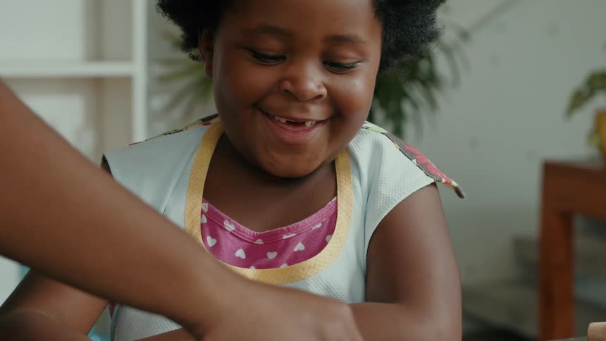 Little girl with happy expression in a kitchen with an adults hand helping her