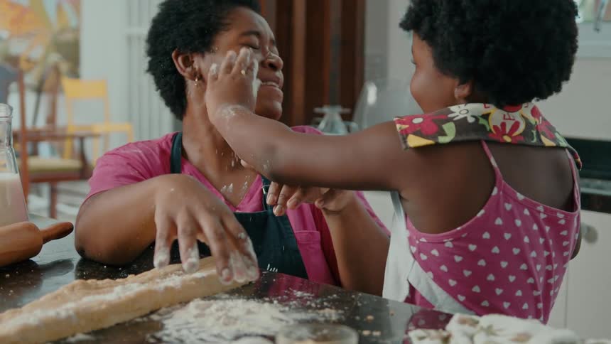 A woman and a child laugh and playfully throw flour at each other while baking together