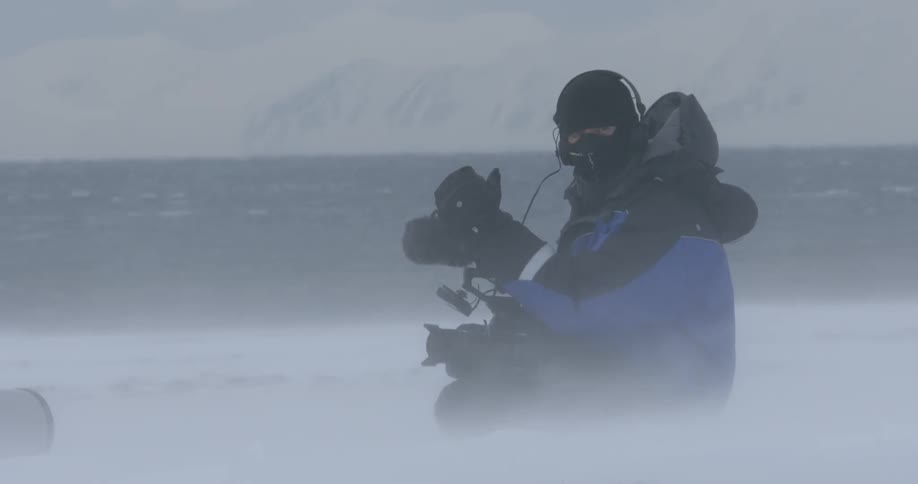 A photographer sits in the snow on a windy day