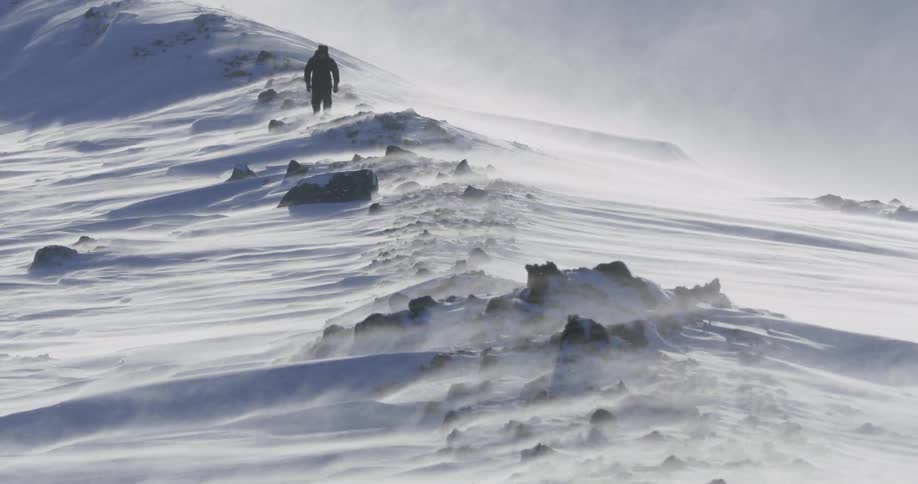 A person hikes along a windy snow covered field