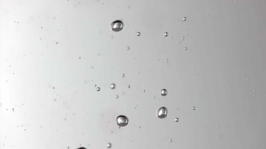 Multiple small clear bubbles float up and down within a liquid against a light gray background