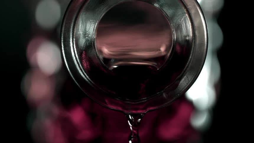 Close up of a red drink poured from a glass bottle opening