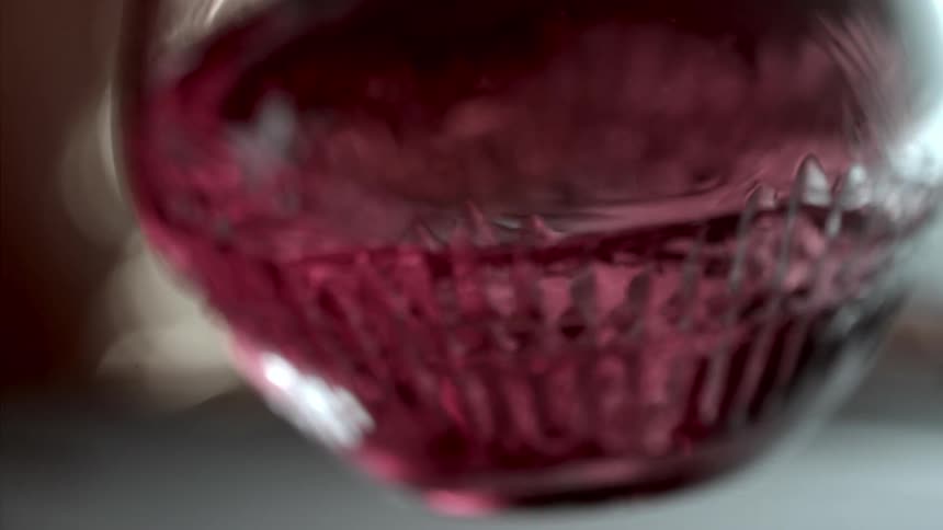 Pink or red liquid swirls inside a glass textured with geometric patterns