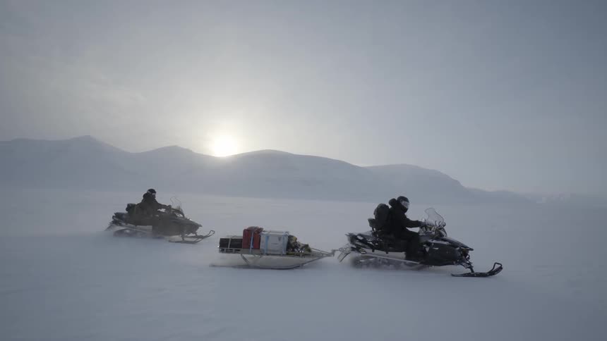 A couple of people on snowmobiles pulling a wagon in the snow