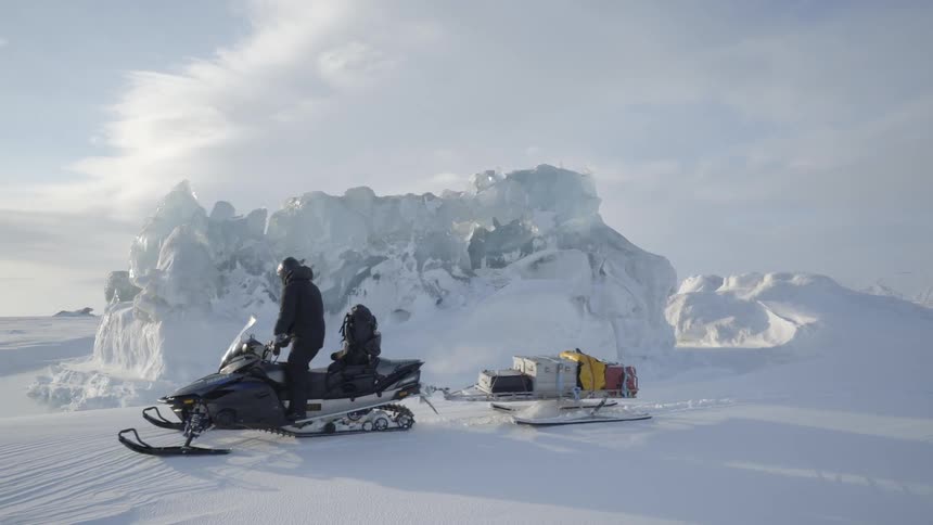 A person drives a snowmobile towing a sled in a frozen landscape