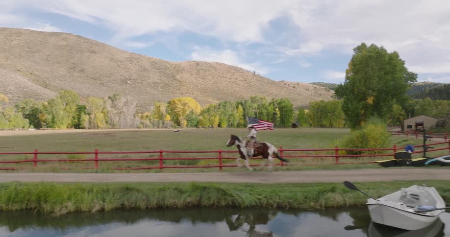 Person on horseback passes a scenic field by a calm canal