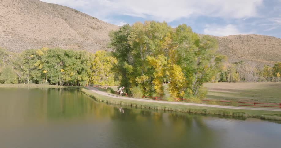 A person rides a horse along a scenic riverside trail lined with trees and hills