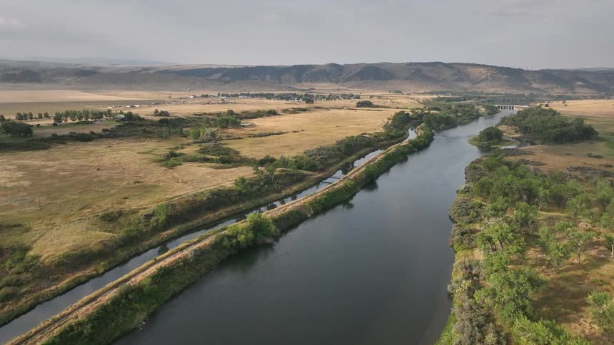 A wide river winds through golden plains with distant hills under a hazy sky
