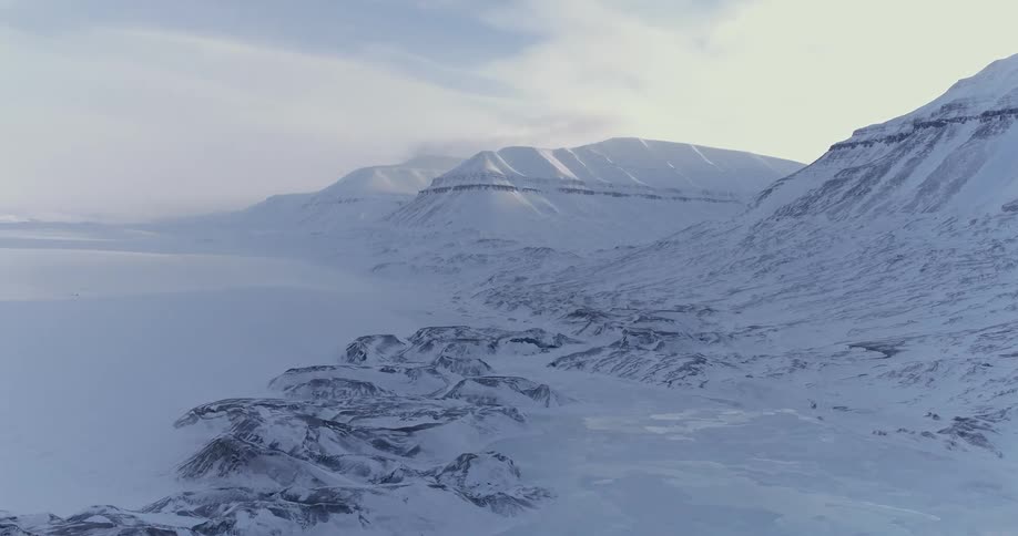 Wispy clouds hang over a snow-covered mountain range and coastline