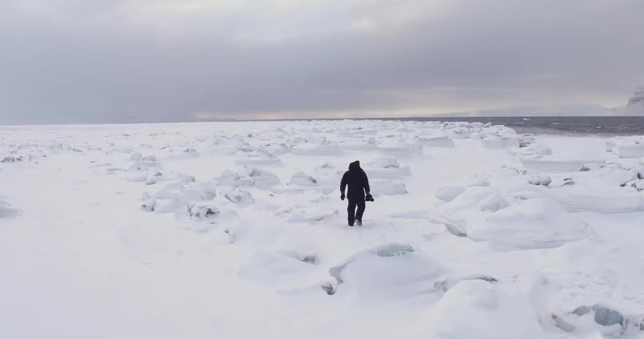 A man is hiking around rocks on a snow covered field