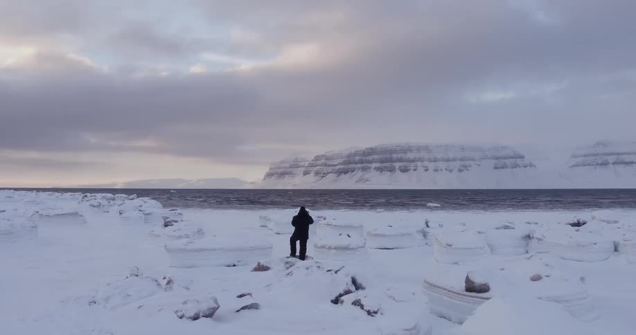 A man stands on a stretch of ice near some water