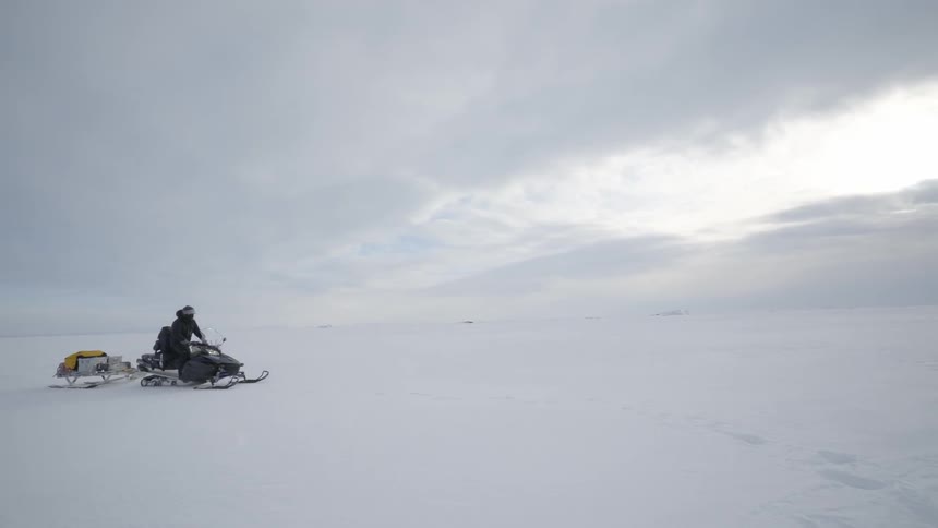 A man is riding a snowmobile on a long field