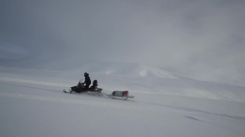 A man drives a snowmobile and supply sled through the snow