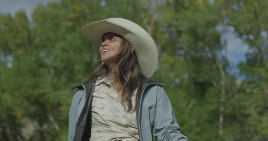 A woman wearing a cowboy hat is riding a horse in spring