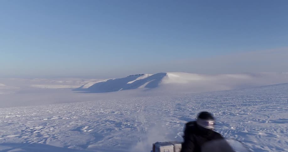 A man driving a snowmobile across a snow covered field