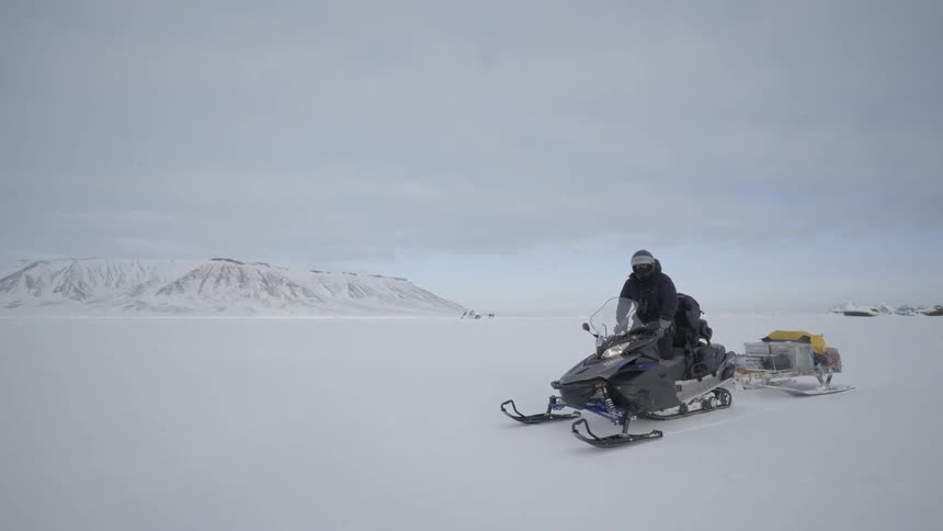 A man on a snowmobile pulling a wagon behind it in the snow
