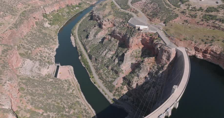Aerial view of a large dam surrounded by rocky cliffs and a winding river