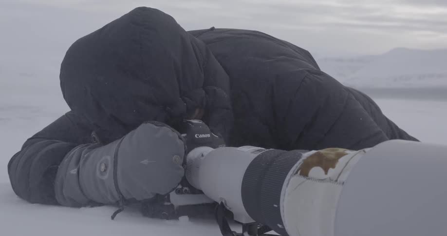 A photographer takes photos with a large lens in the snowy wilderness