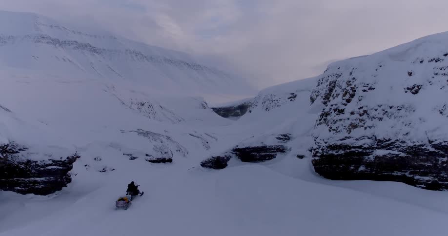 Person riding a snowmobile travels through snowy hills