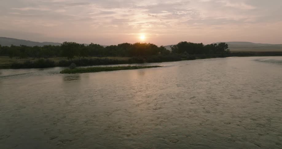 A calm lake sits surrounded by forest under a setting sun