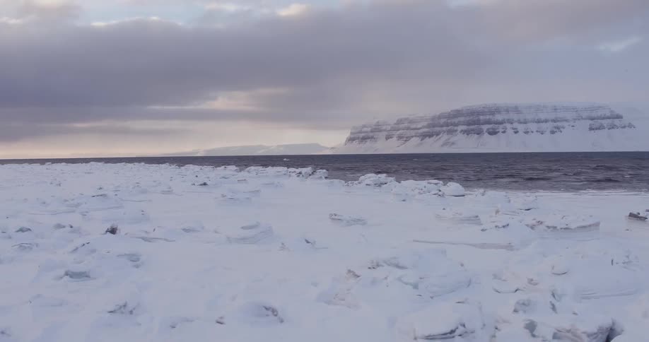 Dark clouds hang over the sea and a frozen landscape