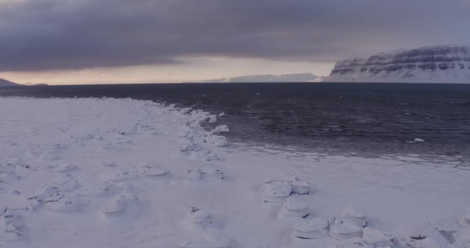 Dark clouds hang over the sea and a frozen landscape
