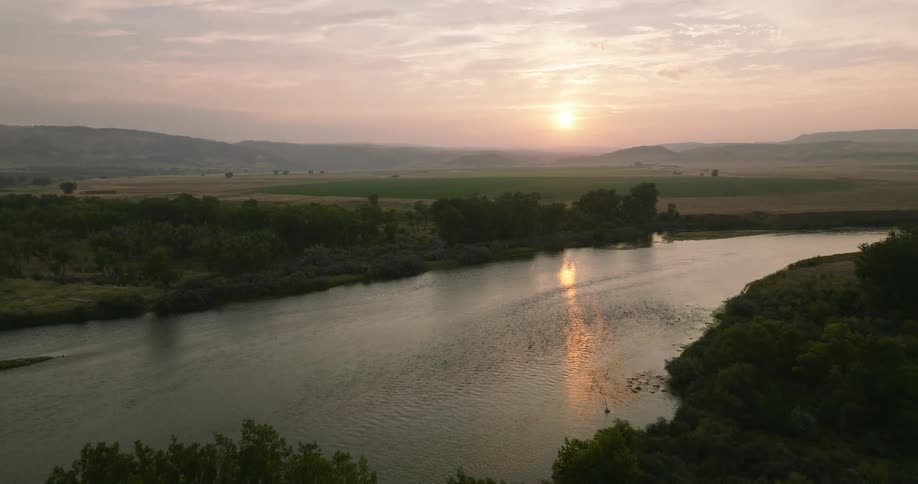 Aerial view of a winding river surrounded by green areas with mountains on the horizon