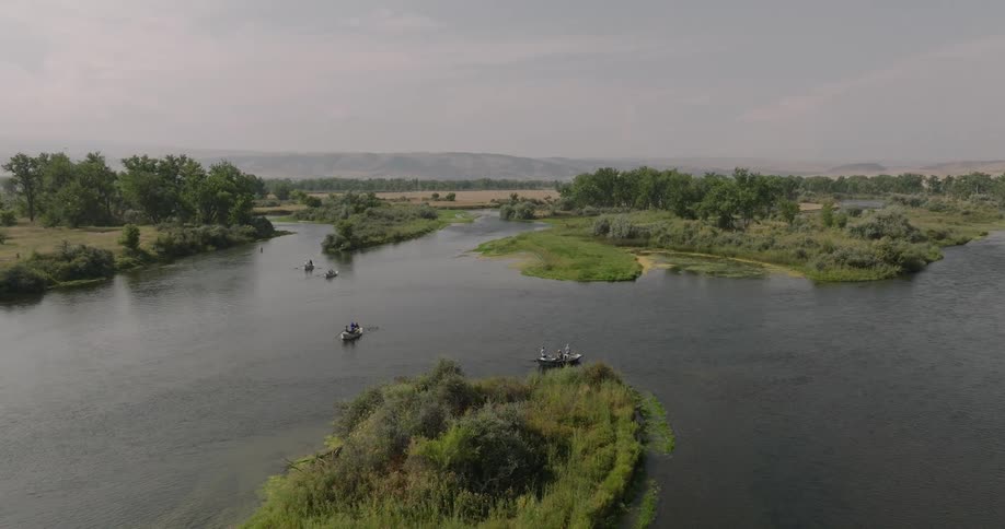 People are fishing from boats on a calm river surrounded by greenery in a rural landscape