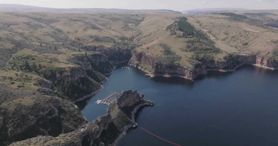 An aerial view shows a large body of water surrounded by steep rocky canyons with a marina nestled in a cove and a floating barrier extending across the water