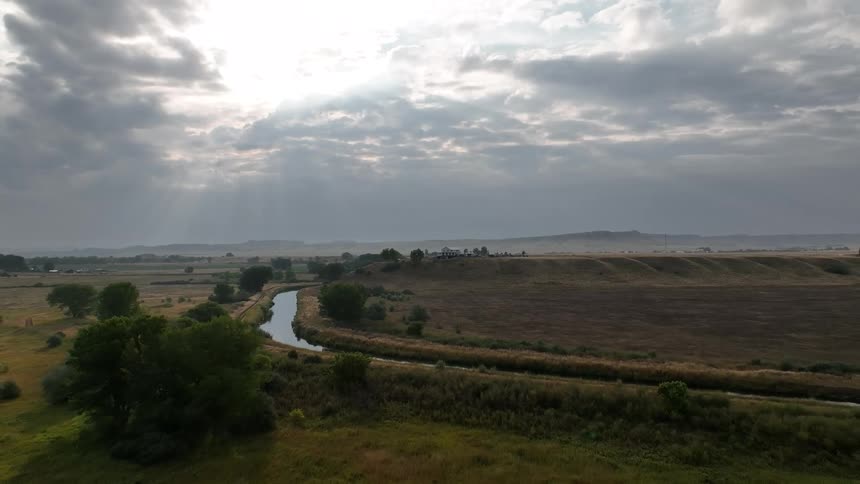 A winding river cutting through misty plains beneath a cloudy sky