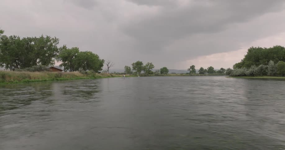 Wide river flows calmly under a cloudy sky with trees lining both banks