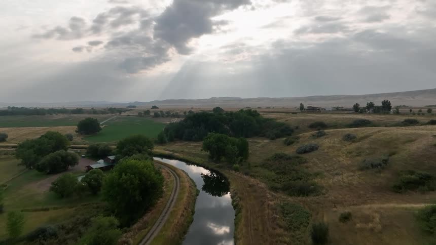 A winding river cuts through a rural landscape under sunlit clouds
